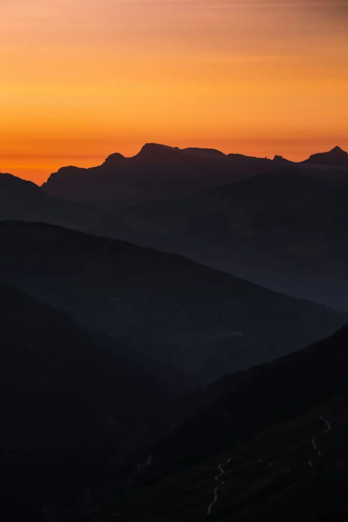 Silhouette des montagnes sous un ciel d'un orange éclatant au crépuscule.