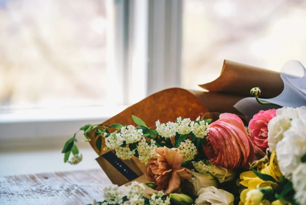 Bouquet élégant avec des renoncules roses et de petites fleurs blanches sur bois.